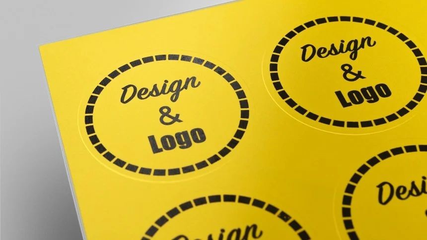etiketa material rumena laser inkjet tiskanje Rumene okrogle nalepke na listu A4 formata. Na nalepkah je natisnjen napis "Design & Logo"