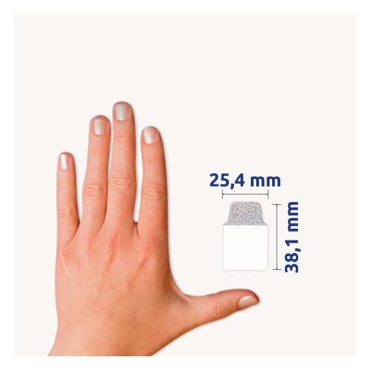 Slika prikazuje roko z urejenimi nohti poleg referenčne merice za predmet, ki ima dimenzije 25,4 mm krat 38,1 mm.