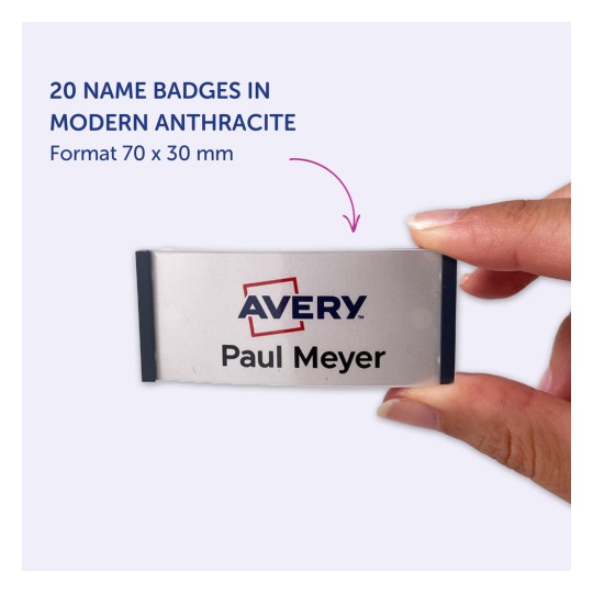 Slika prikazuje roko, ki drži priponko z imenom 'Avery' in imenom 'Paul Meyer', kar kaže, da je del kompleta 20 priponk v moderni antracitni barvi, velikosti 70 x 30 mm.