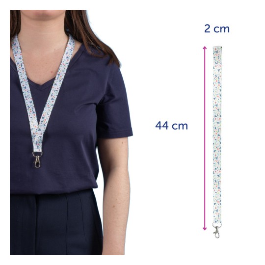 Slika prikazuje osebo z vrvico s cvetličnim vzorcem okoli vratu. Vrvica meri 44 cm v dolžino in 2 cm v širino ter je namenjena za držanje predmetov, kot so ključi ali izkaznice.