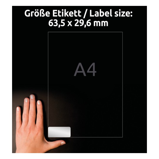 Slika prikazuje roko, ki drži prozorno nalepko z napisom, ki označuje velikost nalepke 63,5 x 29,6 mm, ob referenci velikosti papirja A4.