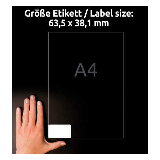 Slika prikazuje nalepko velikosti 63,5 x 38,1 mm ob roki za primerjavo velikosti, v ozadju pa je označen format papirja A4.