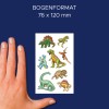 Slika prikazuje roko, ki drži list dinozavrskih nalepk z različnimi dizajni dinozavrov na temno modrem ozadju. Velikost lista je navedena kot 76 x 120 mm.