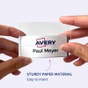 Slika prikazuje osebo, ki drži priponko z imenom 'Paul Meyer' in logotipom Avery, kar nakazuje, da je narejena iz trpežnega papirnatega materiala in je enostavna za vstavljanje.