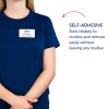 Slika prikazuje osebo, ki nosi mornarsko modro srajco z imenskim kartončkom, na katerem piše 'B. Carlos, Direktor marketinga'. Poleg tega je besedilo, ki opisuje samolepilno lastnost imenskega kartončka, ki navaja, da se zanesljivo drži oblačil in se zlahka odstrani, ne da bi pustil kakršne koli sledi.