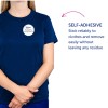 Slika prikazuje osebo, ki nosi majico s kratkimi rokavi v temno modri barvi, na kateri je samolepilna značka z imenom 'B. Carlos DIREKTOR TRŽENJA'. Besedilo na desni strani poudarja samolepilno značilnost, ki izpostavlja njeno zanesljivost in odstranitev brez ostankov.