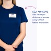 Slika prikazuje osebo, oblečeno v mornarsko modro srajco z imensko značko, na kateri piše 'B. Carlos, DIREKTOR MARKETINGA.' Značka je samolepilna, poleg nje pa je besedilo, ki pojasnjuje njene lastnosti.